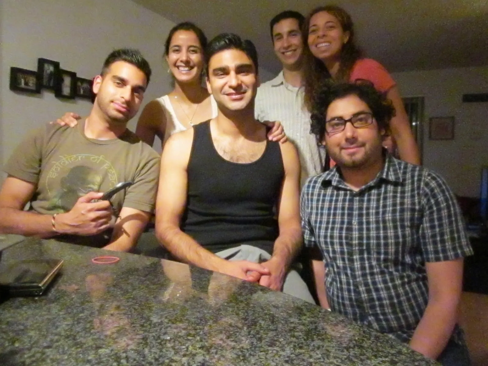 Six friends gathered around a kitchen counter, smiling at the camera