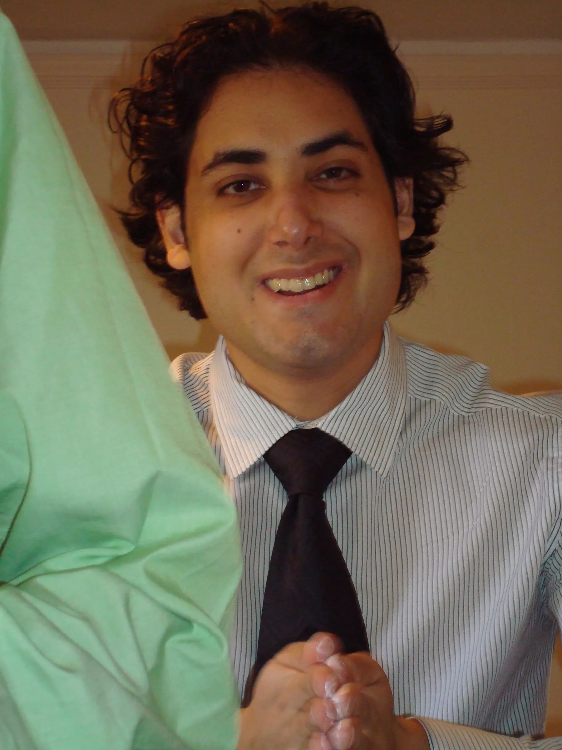 A young man with curly hair smiling, in a shirt and tie