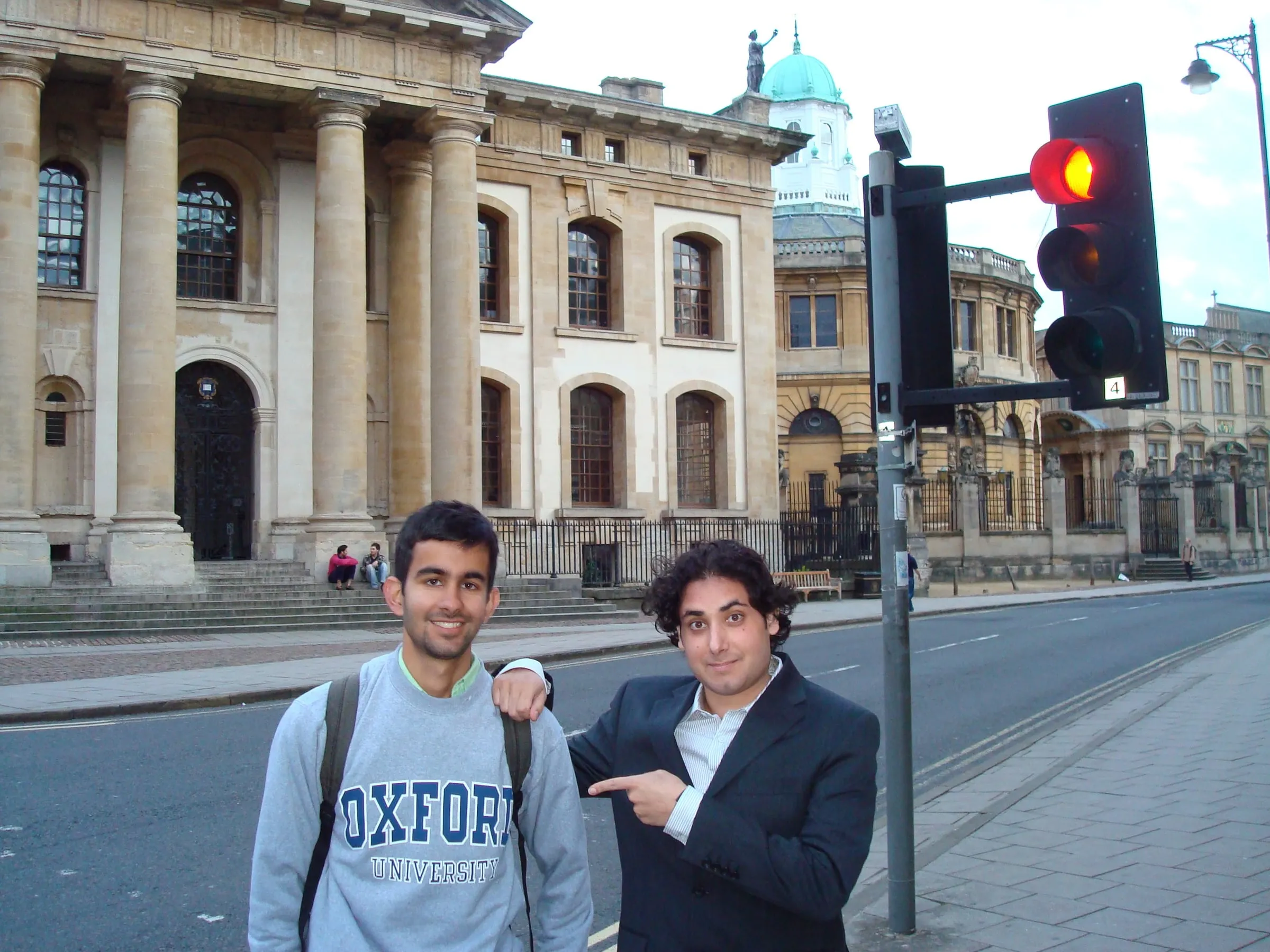 Two young men on a street in Oxford, one in an Oxford sweatshirt, in front of a columned stone building