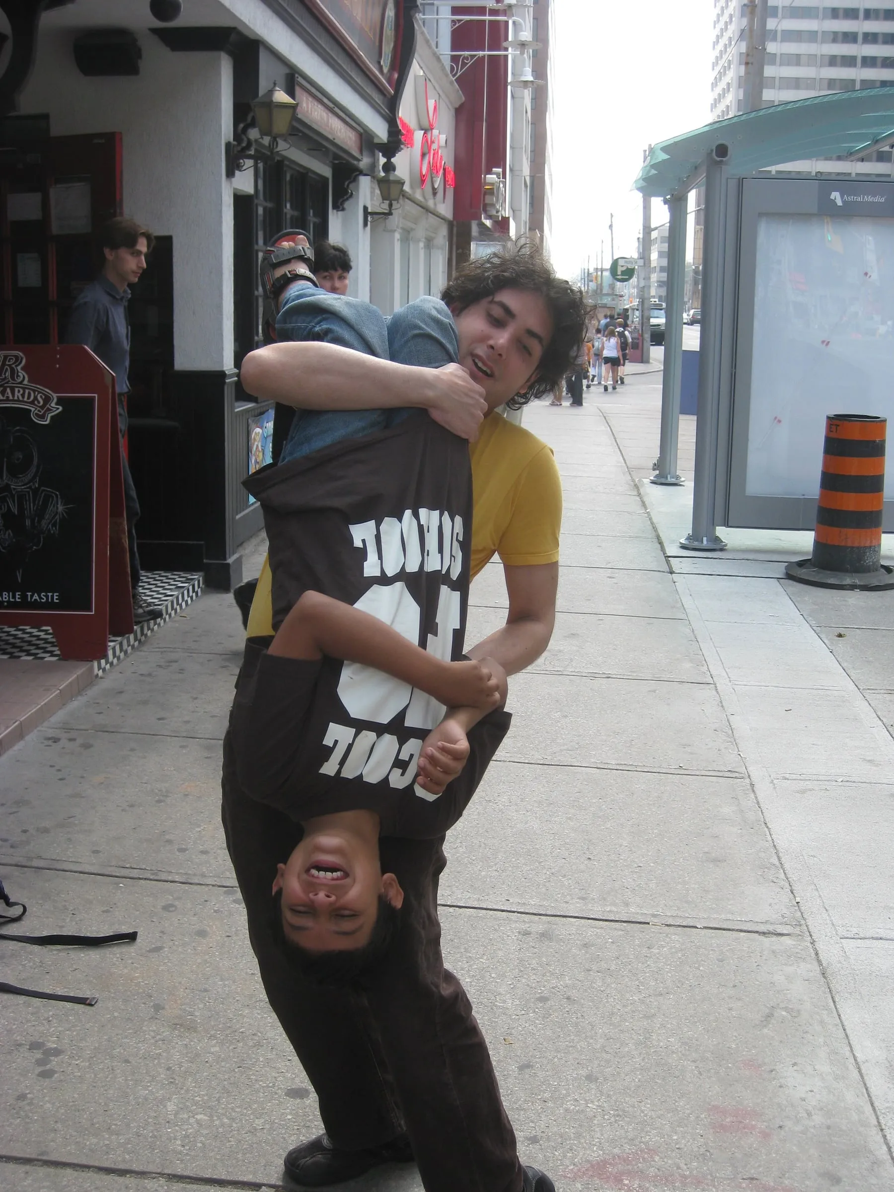 Two young men on a city sidewalk, one holding the other upside down