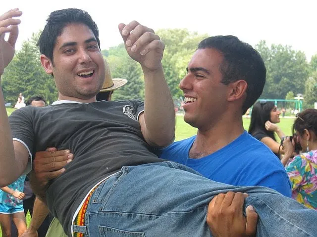 A young man laughing as a friend carries him in his arms in a park