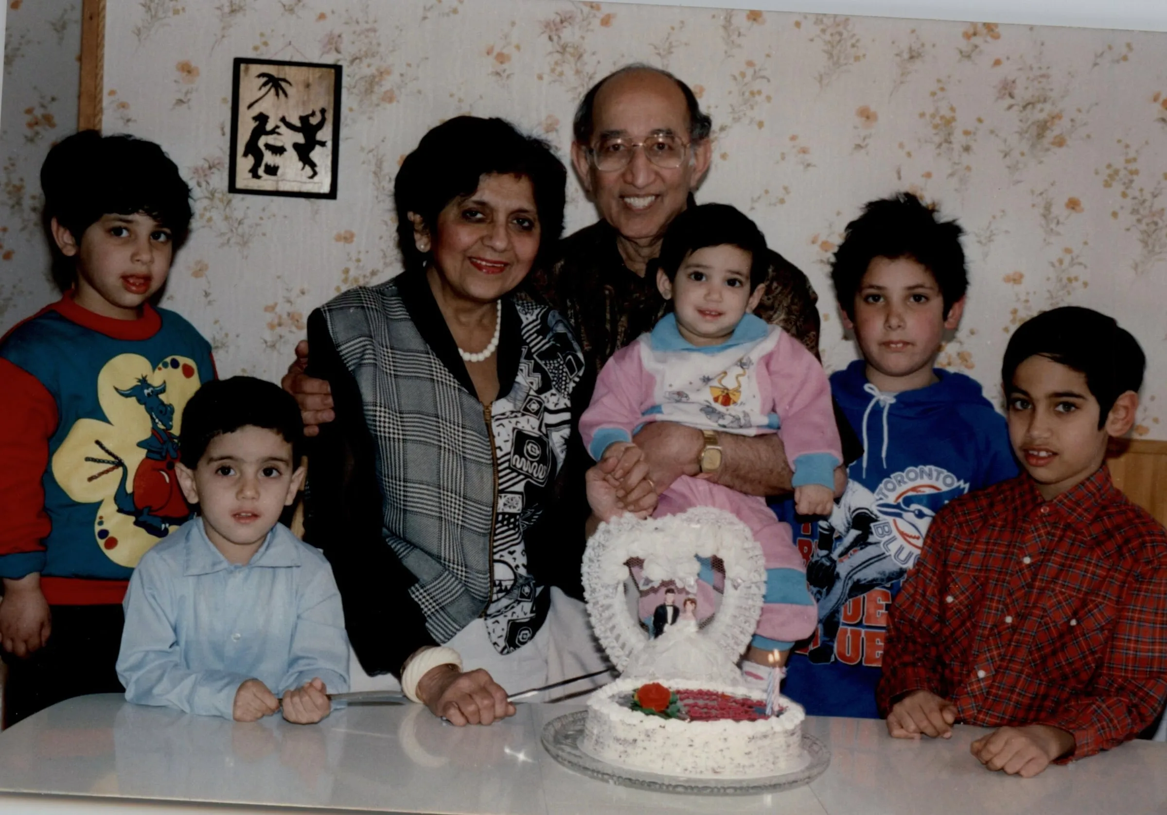 A family around a birthday cake: grandparents holding a toddler, and four boys