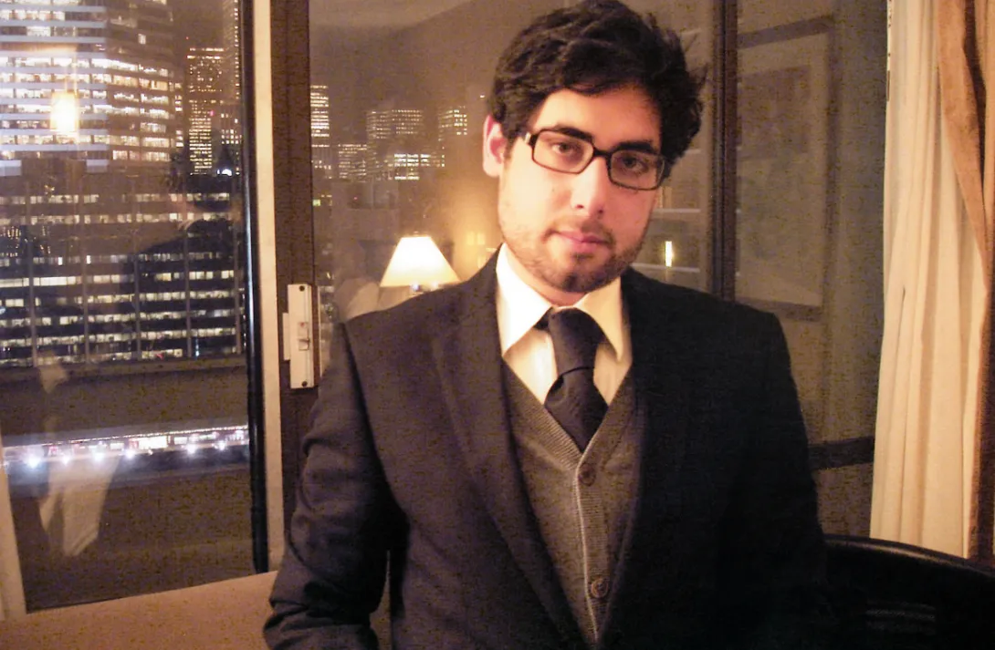 Jehangir in a suit, tie and glasses, city lights behind him